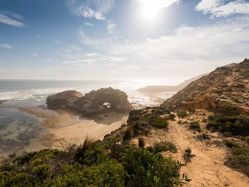 A headland and its beach seen from the clifftop path, sun low over the water