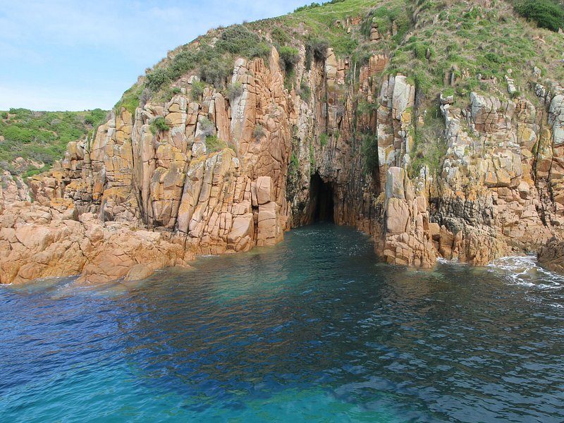 A sea cave cut into a granite headland, turquoise water at its mouth